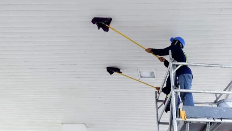 Technician on scaffolding dusting warehouse ceiling — commercial high dusting Tampa FL