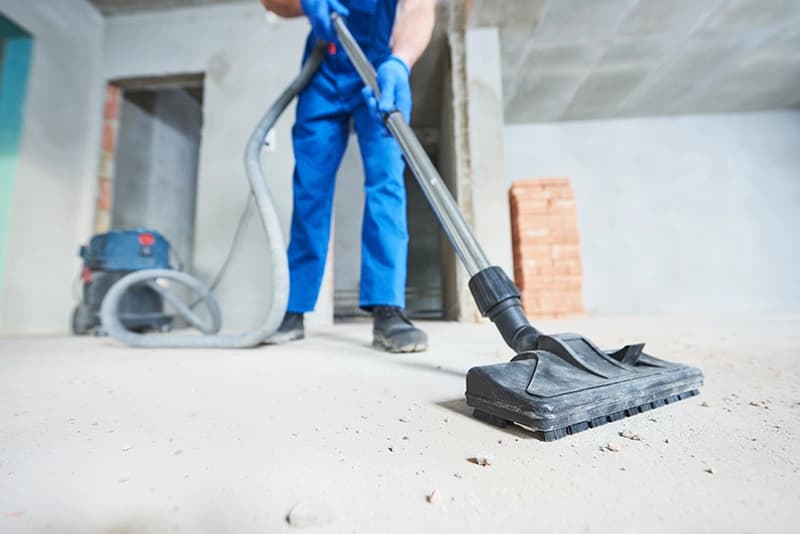 Worker vacuuming construction dust from concrete floor — post-construction cleanup service